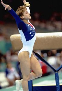 Female gymnast with hands raised over head after finishing a routine